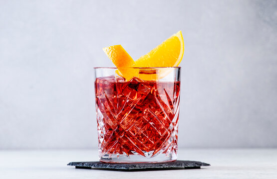 Negroni popular alcoholic cocktail with dry gin, red vermouth and red bitter, orange slice and ice cubes. Gray bar counter background, bar tools, copy space