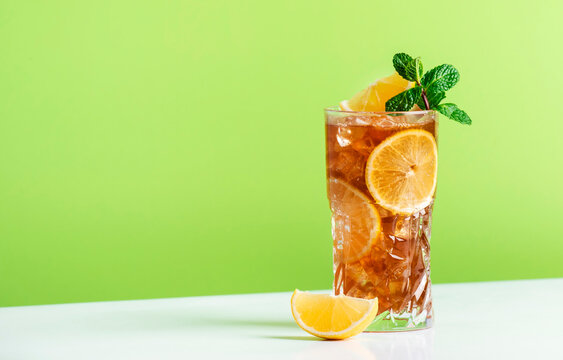 Long Island Ice Tea Cocktail With Vodka, Rum, Tequila, Gin, Liquor, Lemon Juice, Cola And Ice, Garnished With Lemon Slice And Mint In Highball Glass. Green Background