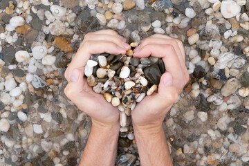 A man makes a heart out of pebbles. Heart on the sea. Romantic photo. Holiday on February 14 on a journey to the ocean.
