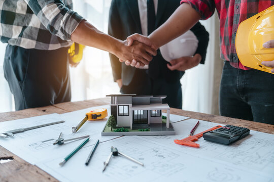 Shaking hands, Blueprints architects and building engineers talking meeting and planning will chronicle the design and technical aspects of a new house construction, renovation remodeling.