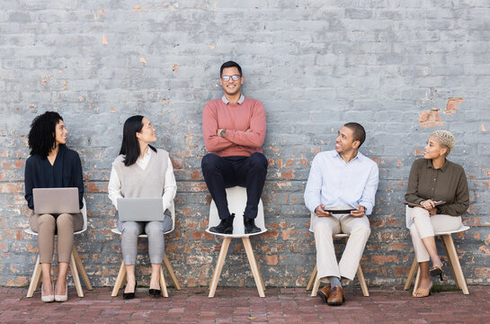 Creative Business People, Waiting Room And Man Standing Out Against A Brick Wall For Interview, Meeting Or Opportunity. Group Of Employee Interns With Technology Looking At Candidate For Startup