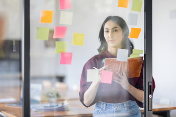 Fototapeta na wymiar Business female employee with many conflicting priorities arranging sticky notes commenting and brainstorming on work priorities colleague in a modern office. 