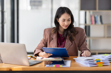Fototapeta premium Freelancer Happy business Asian woman in knitwear taking notes at laptop sitting at desk office, finance concept. 