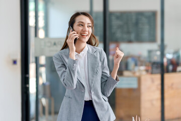 Beautiful Asian woman talking on the phone and excited about successful business event, achieves her intended goal.