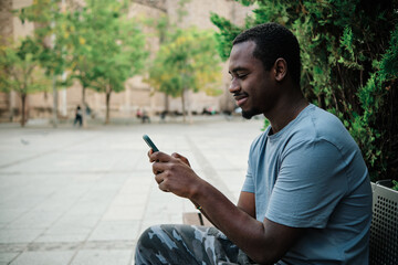 Man using a mobile phone sitting on a bench outdoors.