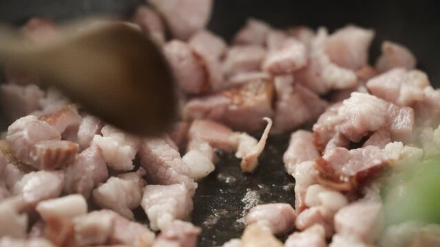 Carbonara recipe; placing fresh garlic clove on hot frying pan next to rendered bacon; melted fat bubbles; close up, 4k, slow motion