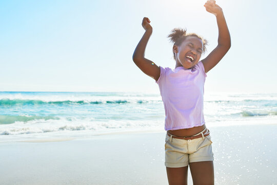 Children, beach and fun with a black girl dancing alone on the sand in summer by the sea or ocean. Nature, kids and blue sky with a female child playing by the water while on holiday or vacation