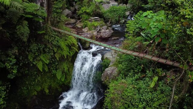 Drone shot of a waterfalls passing a foot bridge