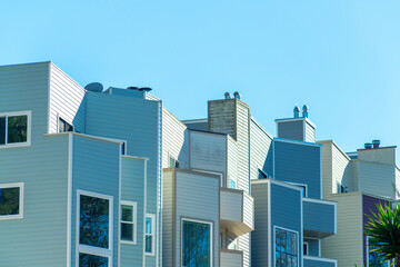 Row of blue and beige wooden townhomes with visible windows and white accent frames and clear blue sky