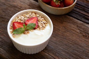 Strawberry yogurt in a wooden bowl with granola, mint and fresh strawberry on wooden background. Health food concept.