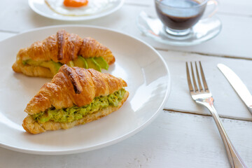 Croissant sandwich with egg,avocado on white dish and honey, coffee. breakfast and healthy food concept
