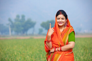 Indian rural women smiling and showing voting sign at agriculture field.