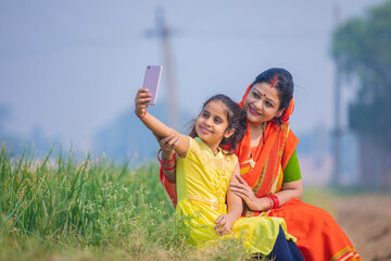 Indian little girl taking selfie with mother at agriculture field.