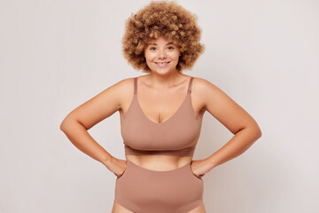 A plus size woman wearing lingerie, smiles happily and holds her hands on her hips, she is proud of her body shape, isolated on a white background