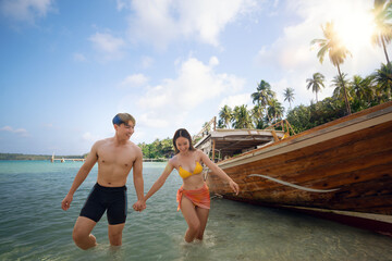 Asian traveller couple sitting and see sunset togather on the beach with longtail boat background