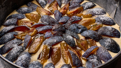 Macro caramelized in sugar syrup pieces of plums in round baking dish on wooden table, panoramic...