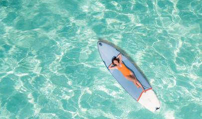 Asian woman in bikini sleep and relax on paddle board on the beach - obrazy, fototapety, plakaty