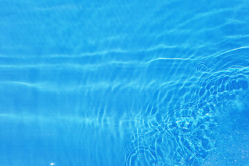 Bluewater waves on the surface ripples blurred. Defocus blurred transparent blue colored clear calm water surface texture with splash and bubbles. Water waves with shining pattern texture background.