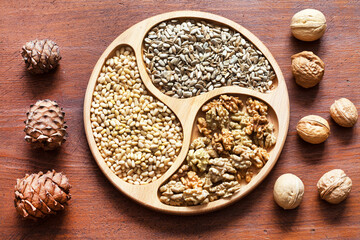 Top view of walnuts, sunflower seeds and pine nuts on a wooden plate. Organic vegetarian healthy food. Cedar cones nearby. Flat lay, close-up, mockup