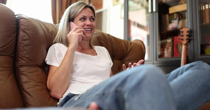 Young smiling woman sitting on sofa talking on mobile phone 4k movie slow motion 