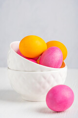 Portion of colourful hand-painted boiled easter eggs of pink and yellow colour served in two ceramic bowls on white wooden table prepared for celebration of  Resurrection Sunday traditional holiday