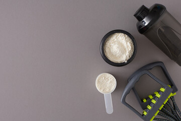 Sports nutrition concept. Flat lay photo made of protein powder in jar with shaker and expander on grey background with copy space. Minimal fitness diet idea.