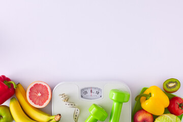 Slimming concept. Flat lay composition of scales with tape measure, dumbbells, fruits and vegetables on white background with copy space. Proper diet idea.