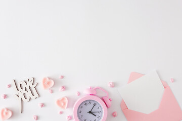 Valentines Day concept. Flat lay photo of pink alarm clock, heart shaped candles, inscriptions love you and envelope with letter on white background with copy space. Lovers holiday card idea.