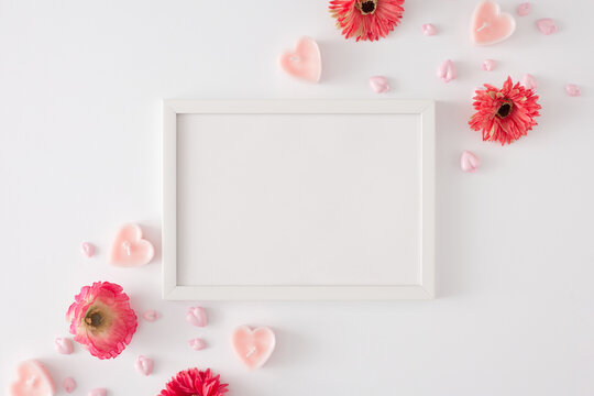 Valentines Day concept. Flat lay composition made of spring flowers, pink heart shaped candles and frame in the middle on white background. Women's day celebration idea.