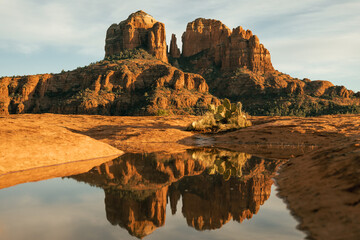 Horizontal image of cathedral rock seen from secret slickrock with reflection of geological sandstone rock formations and spires with cactus and water