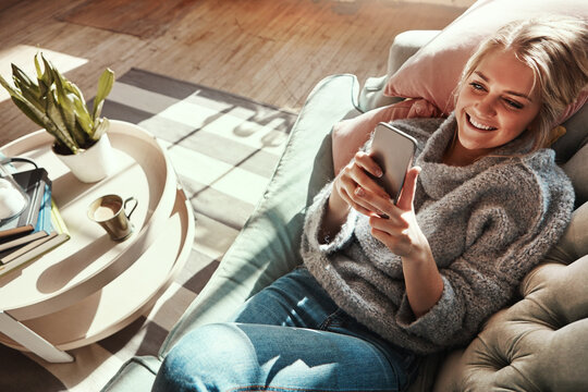 Smile, sofa and woman at home on a phone in a living room calm on social media with happiness. House couch, lounge and person relax on a mobile online on wifi looking happy from streaming web content