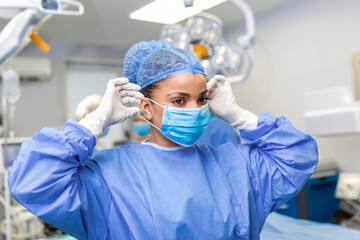 Portrait of beautiful female doctor surgeon putting on medical mask standing in operation room....