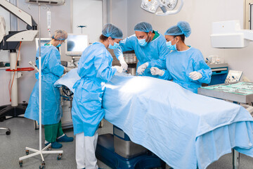 A surgeon's team in uniform performs an operation on a patient at a cardiac surgery clinic. Modern...