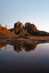 Young beautiful woman standing on rock point looking out at Cathedral Rock in Sedona Arizona USA Southwest at sunset with reflection from small pool.