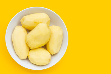 Raw peeled potatoes in white plate on yellow background.