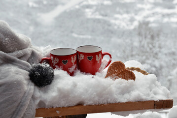 two red mugs with wooden  heart shaped on the snow with blanket on  mountain background