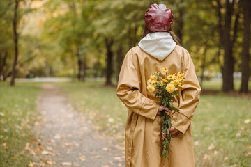 Back view of woman with flower bouquet in park in autumn 