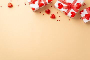 Valentine's Day concept. Top view photo of white gift boxes with ribbon bows heart shaped candies and sprinkles on isolated pastel beige background with copyspace