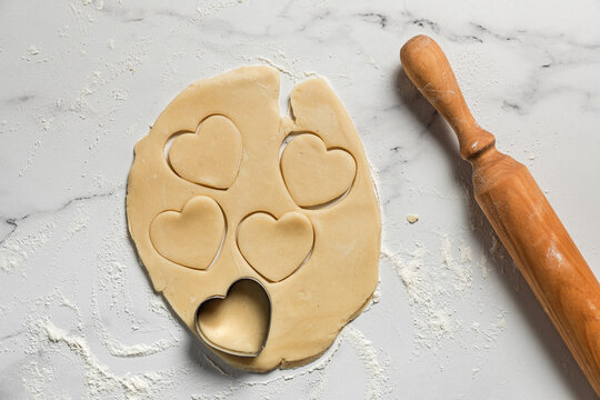 Cutting out heart shaped cookies from rolled out shortbread dough on marble table dusted with flour