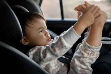 Little toddler girl sitting in car seat and playing with legs, childhood memories and family trip concept