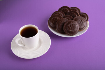 photo a beautiful cup of hot tea on a saucer next to a plate of chocolate-covered cookies