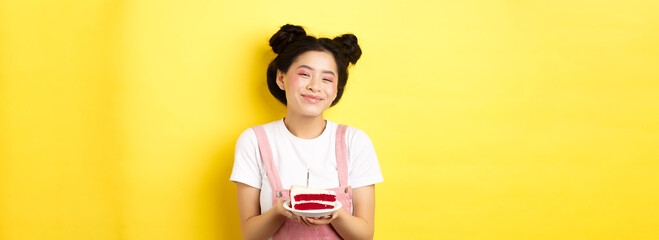 Happy asian birthday girl with bright makeup, blowing candle on cake, making wish, standing on...