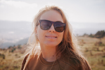 Close-up of the Caucasian woman in the mountains at sunny day in autumn. Smiling woman having a walk. 