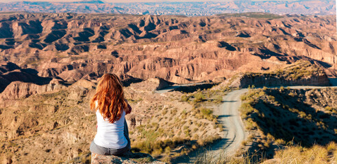 Woman sitting and looking mountain desert and road curve- thinking,  travel,  opportunity concept ( Gorafe desert,  Andalusia in Spain) © M.studio
