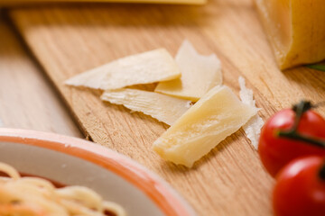 A piece of aged parmesan cheese on a wooden cutting board with a branch of cherry tomatoes, close-up.