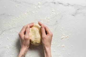 Shortbread cookie dough in woman's hands on marble table dusted with flour before rolling out