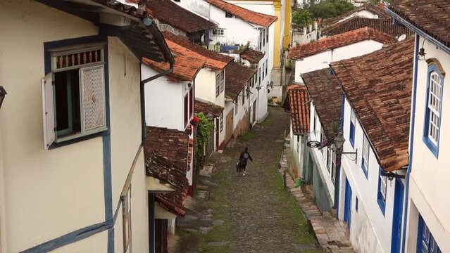 traveler walks down narrow cobbled slope between historic buildings in Ouro Preto, MG, Brazil