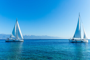 Fototapeta premium sailing yacht boats with white sails in blue sea , seascape of beautiful ships in sea gulf with mountain coast on background