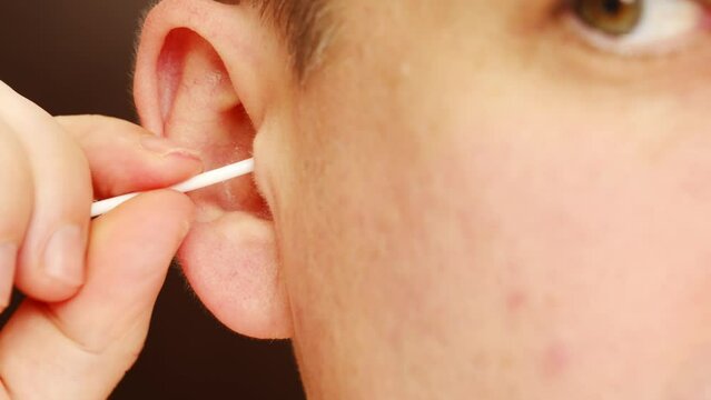 close-up of a man's ear. a man with a cotton swab cleans the ear canals from earwax.