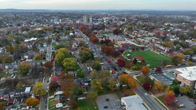 Slow high aerial orbit showing skyline and outskirts of small city in America during autumn. Changing leaves during fall and beautiful cityscape.